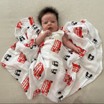 Baby wrapped in a British design muslin swaddle with black cabs and london buses