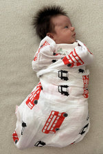 Newborn baby swaddled in a British pattern white muslin blanket with london black cab and buses UK